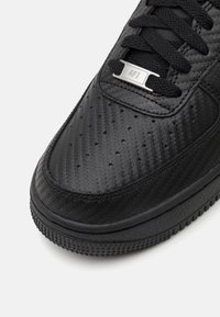 Black sneaker featuring a textured upper with perforations, flat laces, and a metallic accent labeled "AF1." Rubber outsole with a patterned design.