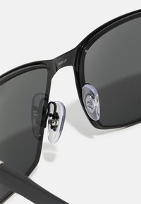 Ochelari de soare negri cu lentile întunecate, formă rectangulară, cu perne de nas transparente și reglabile, și detalii din metal argintiu pe ramă.