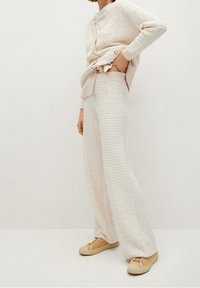 Beige gebreid vest met textuur en knopen, gecombineerd met bijpassende wijde broekspijpen. De outfit heeft een losse pasvorm en wordt gedragen met lichtbeige sneakers.