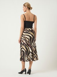 Un haut noir à bretelles associé à une jupe midi en satin à motif zèbre marron et crème, complété par des chaussures à talons hauts noires.