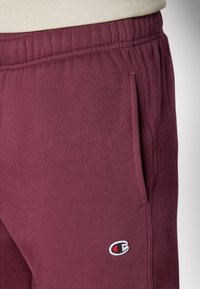 Pantalons de survêtement en coton bourgogne avec une taille élastique et des poches latérales, arborant un petit logo brodé près de la poche gauche.