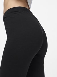 Sorte stretchy leggins med en glatt tekstur, med høy midje og figurnær design, vist fra en sidevinkel.