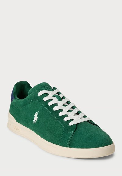 Sneaker verde din suede, cu șirete albe și o talpă din cauciuc crem. Prezintă un toc albastru și un logo alb pe lateral. Textură netedă.