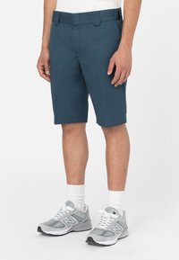 Bermuda blu navy realizzate in un tessuto liscio, con una vita piatta, passanti per la cintura e un taglio sartoriale, abbinate a sneakers grigie sportive.