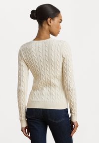 Krema pletena jopica z ribastimi manšetami in spodnjim robom. Ima oprijet kroj in teksturiran vzorec. Nosi se z temnimi jeansa.