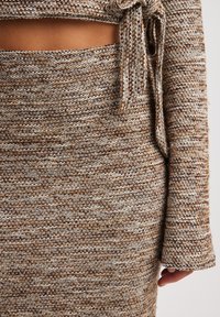 Completo in maglia a due pezzi con top corto dotato di fiocco e gonna abbinata, entrambi in un motivo testurizzato beige e marrone.