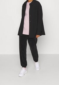 Svart skjorta med knappar ovanpå en ljusrosa t-shirt, tillsammans med svarta ribbstickade byxor och vita sneakers. Enkel design med avspänd passform.