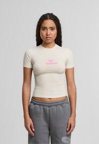Bežs īsām piedurknēm krekls ar rozā "felicious" logotipu priekšpusē, kopā ar pelēkiem sporta biksēm. Gluda auduma ar pieguļošu dizainu.