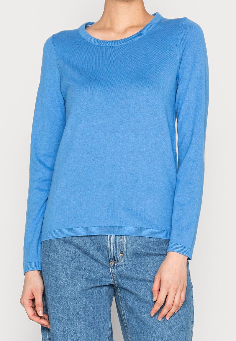 Maglione blu a maniche lunghe realizzato in morbido tessuto a maglia. Presenta un collo a giro e bordi a coste. Abbinato a jeans in denim azzurri.