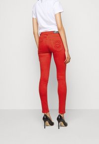 Jeans ajustados rojos de denim elástico, con bolsillos traseros con detalles bordados. Combinados con una camisa blanca y tacones altos negros.