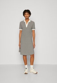 Gestreiftes Polokleid in Schwarz und Weiß mit einem Kragen und kurzen Ärmeln. Getragen mit weißen Sneakers und Socken.