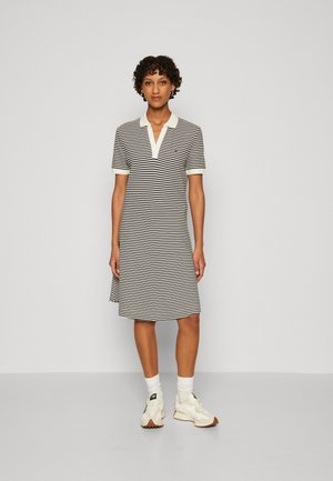 Abito polo a righe in bianco e nero, con colletto e maniche corte. Indossato con sneaker bianche e calze.