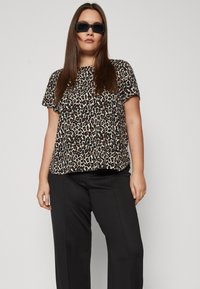 Luipaardprint blouse met korte mouwen, gemaakt van zachte stof, met een losse pasvorm en ronde halslijn, gecombineerd met op maat gemaakte zwarte trousers.