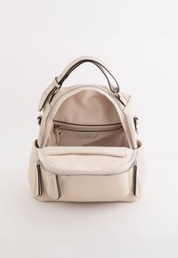 Bolso de cuero beige con cierre de cremallera, dos bolsillos laterales y un bolsillo interior con cremallera. Exterior suave y forro de tela. Correa ajustable incluida.
