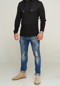 Hoodie noir en maille avec un logo sur le devant, associé à un jean bleu clair déchiré. Des bottines tanner complètent la tenue.