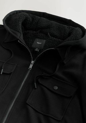 Must mustaga kapuutsiga, millel on tekstureeritud, fliisvoodriga kapuuts, reguleeritav nöör ja kaks esist pocketit. sees on logo etikett.