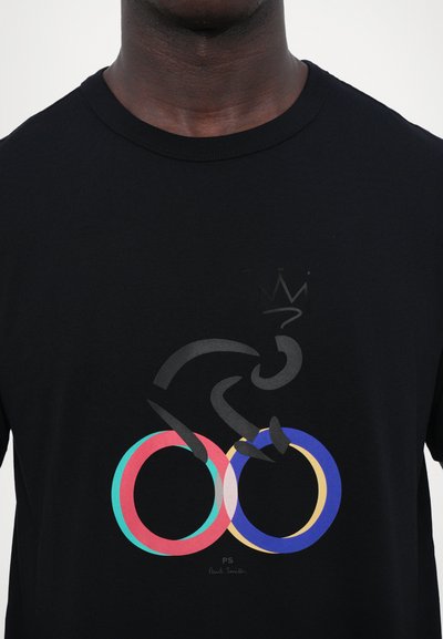 T-shirt noir en coton avec un design coloré de deux anneaux entrelacés et la silhouette d'un cycliste ; signature "PS" sous le graphique.