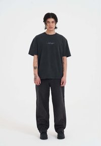 Sort bomulds T-shirt med en afslappet pasform, der har korte ærmer og et lille broderet design på brystet. Båret med mørke, oversized jeans.