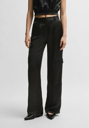 Black satin cargo pants with a high waist, featuring front pleats, two side pockets, and a wide-leg cut. Smooth texture and sleek design.