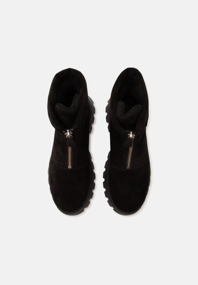 Paire de bottines noires avec fermetures éclair métalliques à l’avant et semelles épaisses en caoutchouc, vues de dessus sur un fond clair.