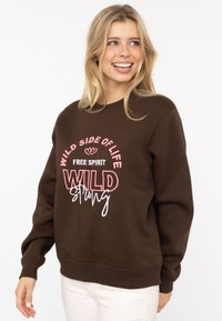 Brązowa bluza z ribbowymi mankietami i dół, z kolorowym haftowanym napisem: "DZIKIE STRONY ŻYCIA," "WOLNY DUCH," oraz "DZIKIE SILNE."