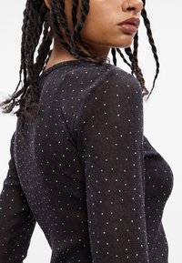 Blusa de manga larga negra con un material de punto texturizado y lunares blancos dispersos. El diseño ajustado resalta la silueta.