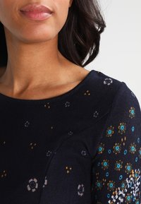 Marinblå långärmad topp med blommönster i blått, vitt och gult. Mjuk tygkvalitet med rund halsringning och lätt struktur på ärmarna.