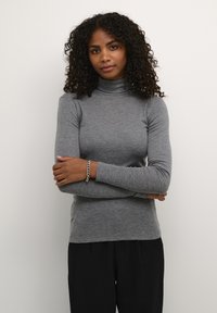 Grauer Rollkragensweater aus einem weichen, elastischen Stoff, mit langen Ärmeln und einer figurbetonten Passform, kombiniert mit dunklen, lockeren Hosen.