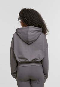 Szara krótka hoodie z kapturem, luźny krój i ściągacz. Wykonana z miękkiego materiału; posiada opadające ramiona i tylny widok. Połączona z dopasowanymi spodniami.