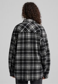 Svart och vit rutigt flanellskjorta med knapp-down krage, neddragna axlar och avslappnad passform, som visar upp ett mjukt, strukturerat tyg.