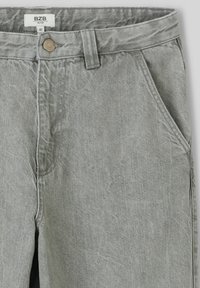 Pantalons en denim gris avec fermeture à bouton, passants de ceinture et poches latérales. Le tissu a une finition lisse et texturée. L'étiquette indique "BZB" et taille 40.