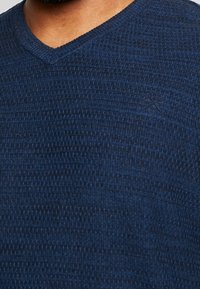 Navy blue V-neck sweater made from textured knit fabric, featuring a subtle pattern and a small logo detail on the lower left side.