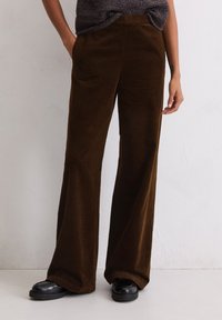 Bruine corduroy wijde broek met verticale ribbels, voorzien van zijzakken en een gladde tailleband, gecombineerd met zwarte loafers.