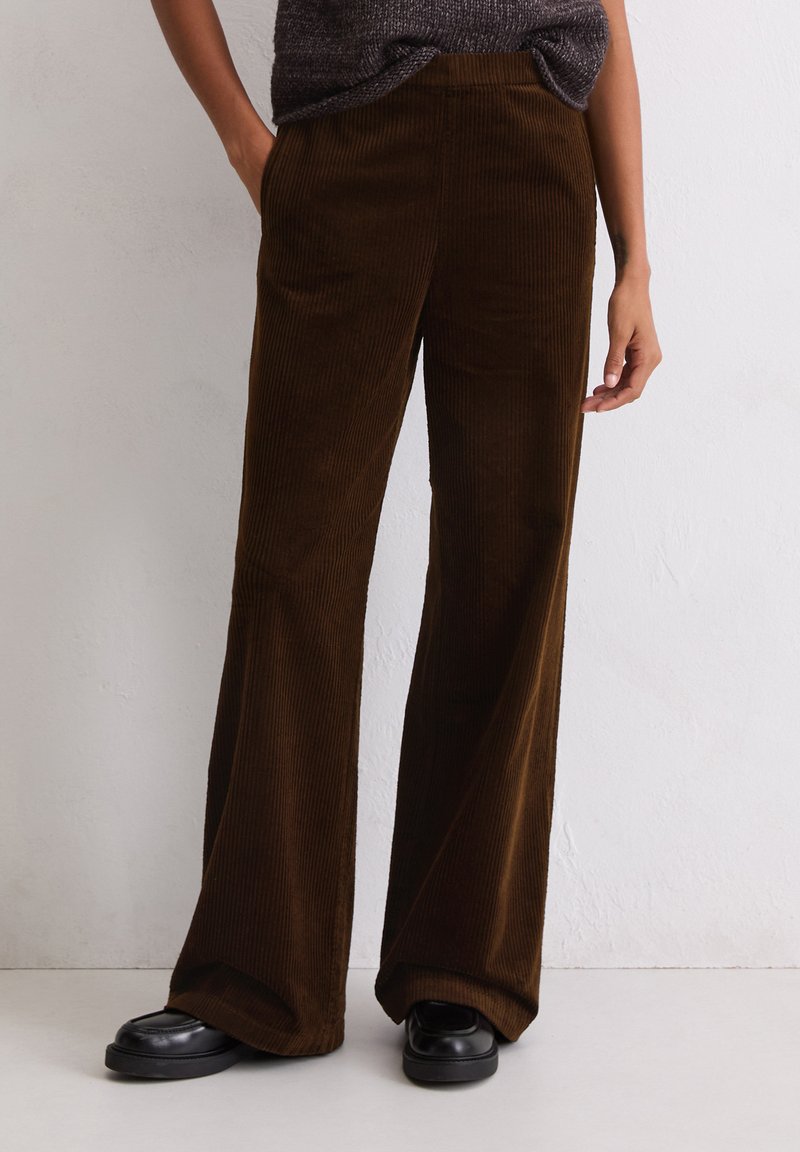 Bruine corduroy wijde broek met verticale ribbels, voorzien van zijzakken en een gladde tailleband, gecombineerd met zwarte loafers.