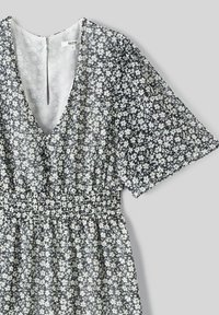 Robe florale gris foncé avec de petites fleurs blanches, manches courtes, décolleté en V profond, taille élastique et détail de fente dans le dos.