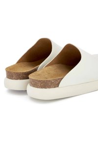 Chaussures blanches à enfiler avec une tige en cuir lisse, un contrefort en liège et une semelle en caoutchouc blanche. Présentent un arrière ouvert et un design à bout arrondi.