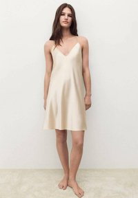 Abito in satin beige chiaro con scollatura a V e spalline sottili, con una silhouette A-line fluida e una texture liscia e morbida.