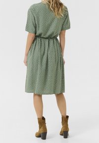 Grön klänning med prickar, korta ärmar och elastisk midja, tillverkad av lätt material. Matchad med bruna ankelskor och en strukturerad klack.