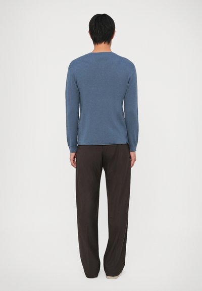 Ριχτός μάλλινος πουλόβερ με μακριά μανίκια σε χρώμα γαλάζιου πέτρας, συνδυασμένος με σκούρους καφέ παντελόνες φαρδιάς γραμμής. Λείος υφάνσιμος με στρογγυλή λαιμόκοψη και στενές μανσέτες.