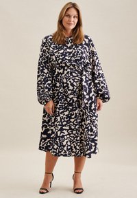 Robe à motifs bleu marine et crème avec des manches longues, une taille ceinturée et une longueur mi-mollet. Fabriquée en tissu doux avec une coupe ample.