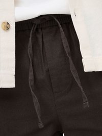 Veste blanche texturée avec bouton portée sur un pantalon noir à taille réglable par cordon et coutures visibles sur les poches avant.