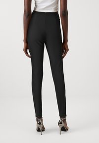 Pantalons noirs côtelés taille haute à coupe slim, dotés d'un détail en trou de serrure à l'arrière, accompagnés de chaussures à talons hauts argentées brillantes.