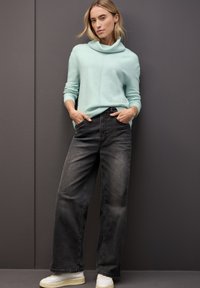 Jasnoniebieski sweter z golfem, z prążkowanymi mankietami, w połączeniu z czarnymi, dżinsowymi spodniami o szerokim kroju z wysokim stanem i białymi sneakersami. Proste, czyste linie.