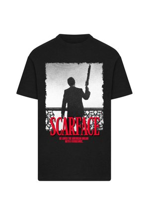 Maglietta nera con grafica in bianco e nero di un uomo che tiene un fucile su un balcone, testo rosso "SCARFACE" e slogan sottostante.