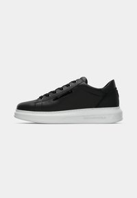 Adidași negri din piele cu talpă din cauciuc albă, profil jos, design cu șireturi și logo embosat; textură netedă și stil minimalist.