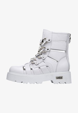 Stivaletto alla caviglia in ecopelle bianca con dettagli in argento, design con lacci, accenti intagliati e una suola spessa e texturizzata per un'altezza aggiuntiva.