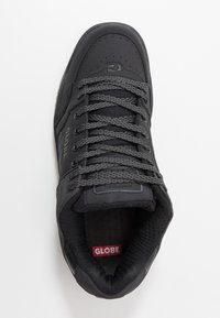 Sneaker nera con parte superiore sintetica, collare imbottito, lacci grigi, punta perforata e logo rosso "GLOBE" sulla linguetta. Suola in gomma visibile.