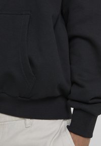 Felpa blu navy con tasca frontale, polsini e orlo a costine. Tessuto morbido, primo piano che mostra i dettagli delle cuciture. Indossata con pantaloni chiari.