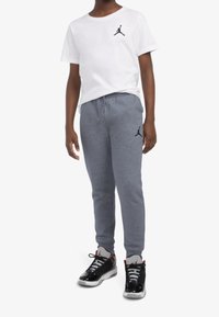 Biała bawełniana koszulka z czarnym logo Jordana, zestawiona z szarymi spodniami dresowymi z czarnym logo oraz czarnymi sneakersami z czerwonymi akcentami.