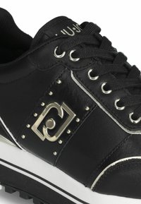 Schwarze Ledersneaker mit silbernen Akzenten, runden Schnürsenkeln, Nietenverzierung und einer weißen Sohle mit schwarzem Profil und kontrastierenden Nähten.